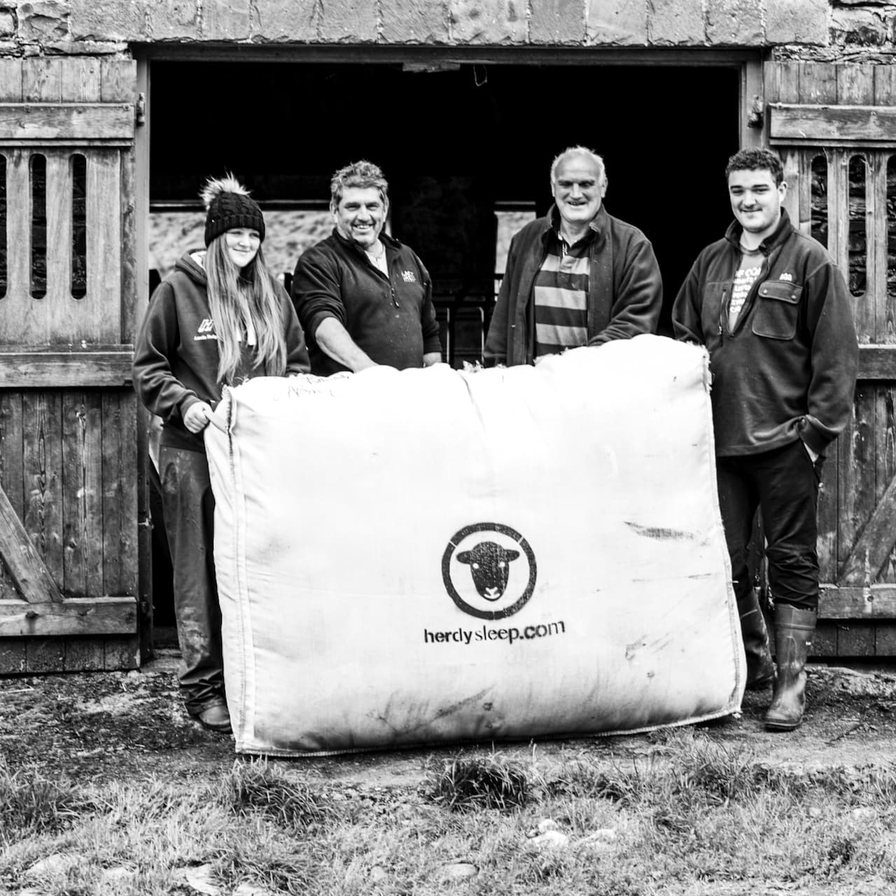 four Herdwick farmers holding a large woven bag filled with Herdwick fleeces