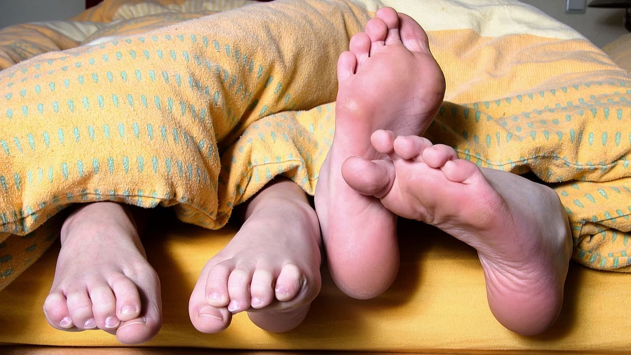 two pairs of feet pocking out from under a yellow duvet